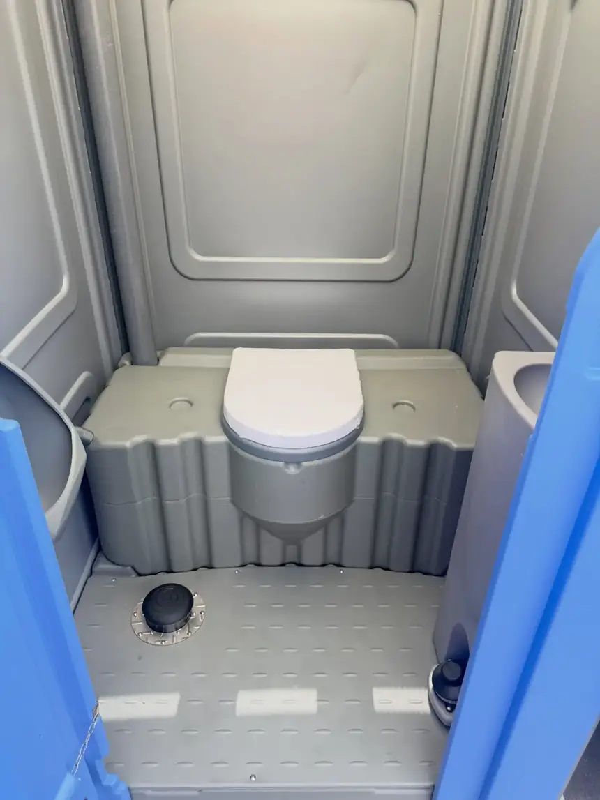 Inside a standard porta potty showing the toilet seat and tank
